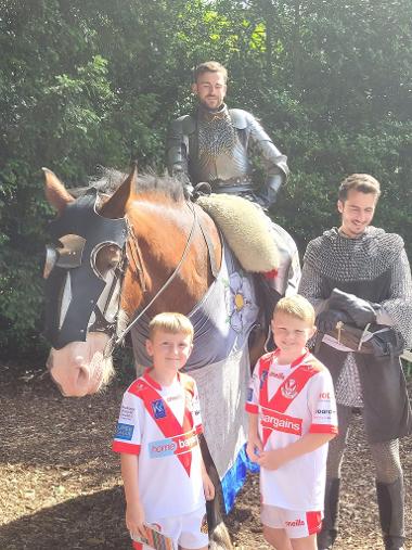 Two children wearing Saints shirts stand in front of a hose and two knights