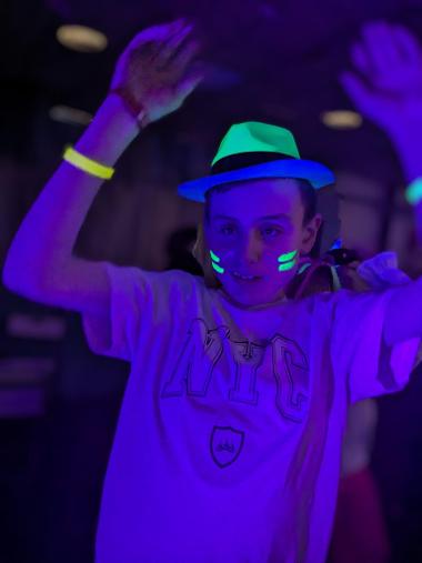A young person wearing a hat and UV paint on their face