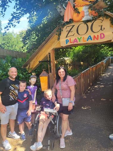 Two children and two adults stand in front of the sign to Zog Playland
